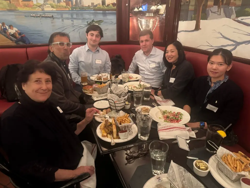 Six guests smiling around a dinner table in a booth at the Penn Club of New York